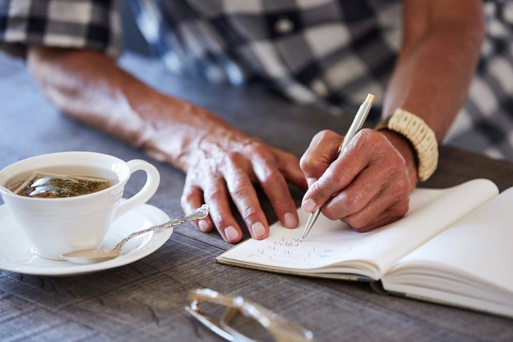 Senior African American woman at home writing in a journal and drinking tea.