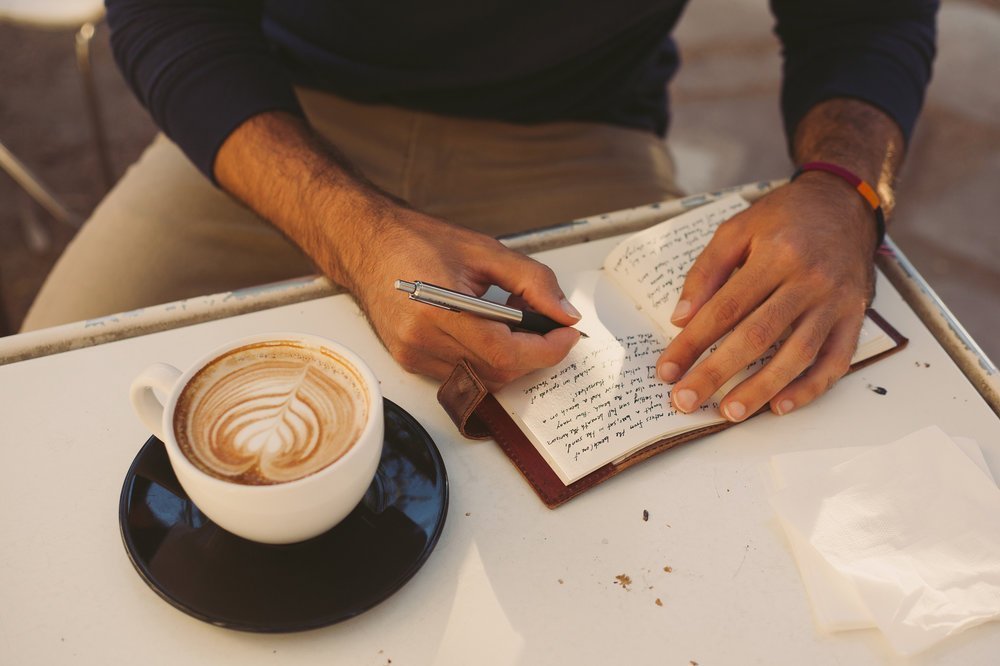 A man writing in a journal while drinking coffee.