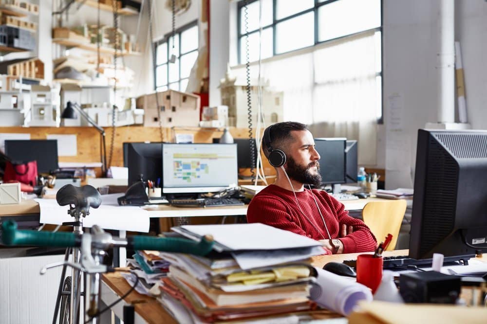 Thoughtful mid adult businessman wearing headphones while sitting at computer desk in office.