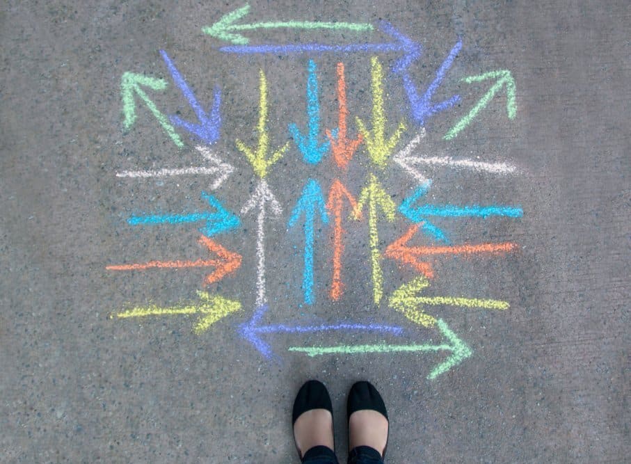 A person standing next to a chalk drawing of arrows going in all directions.