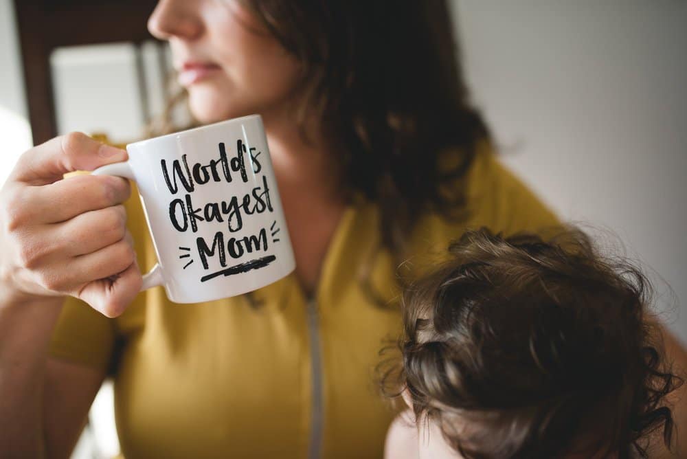 A woman holding a child and a mug that says "worlds okayest mom".