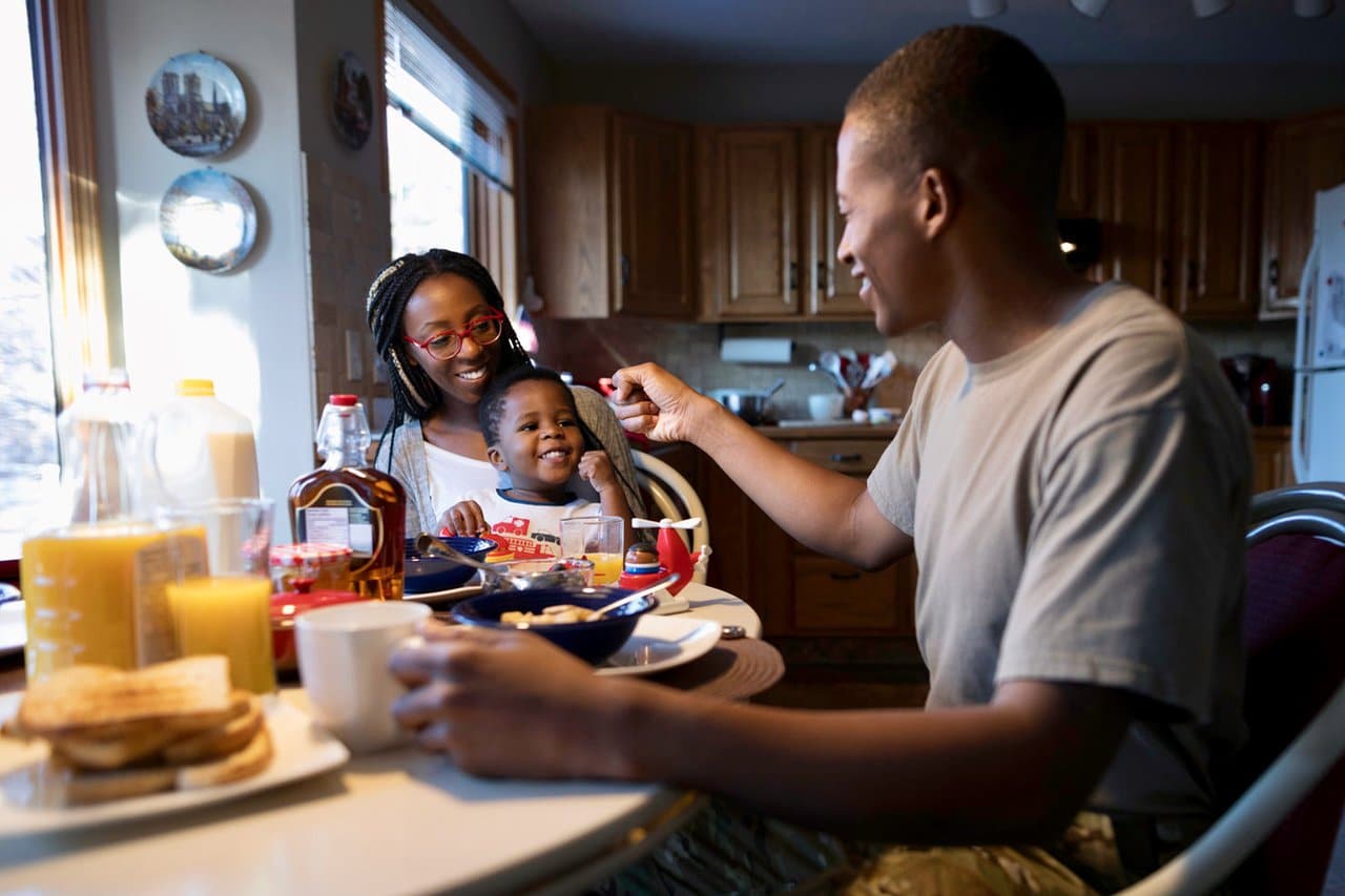 A family with their child interacting and smiling around a breakfast table.