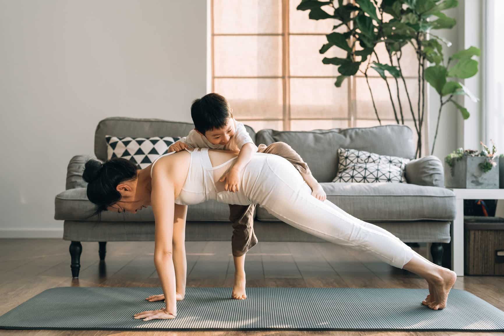 A woman practicing yoga while her child tries to climb on her.