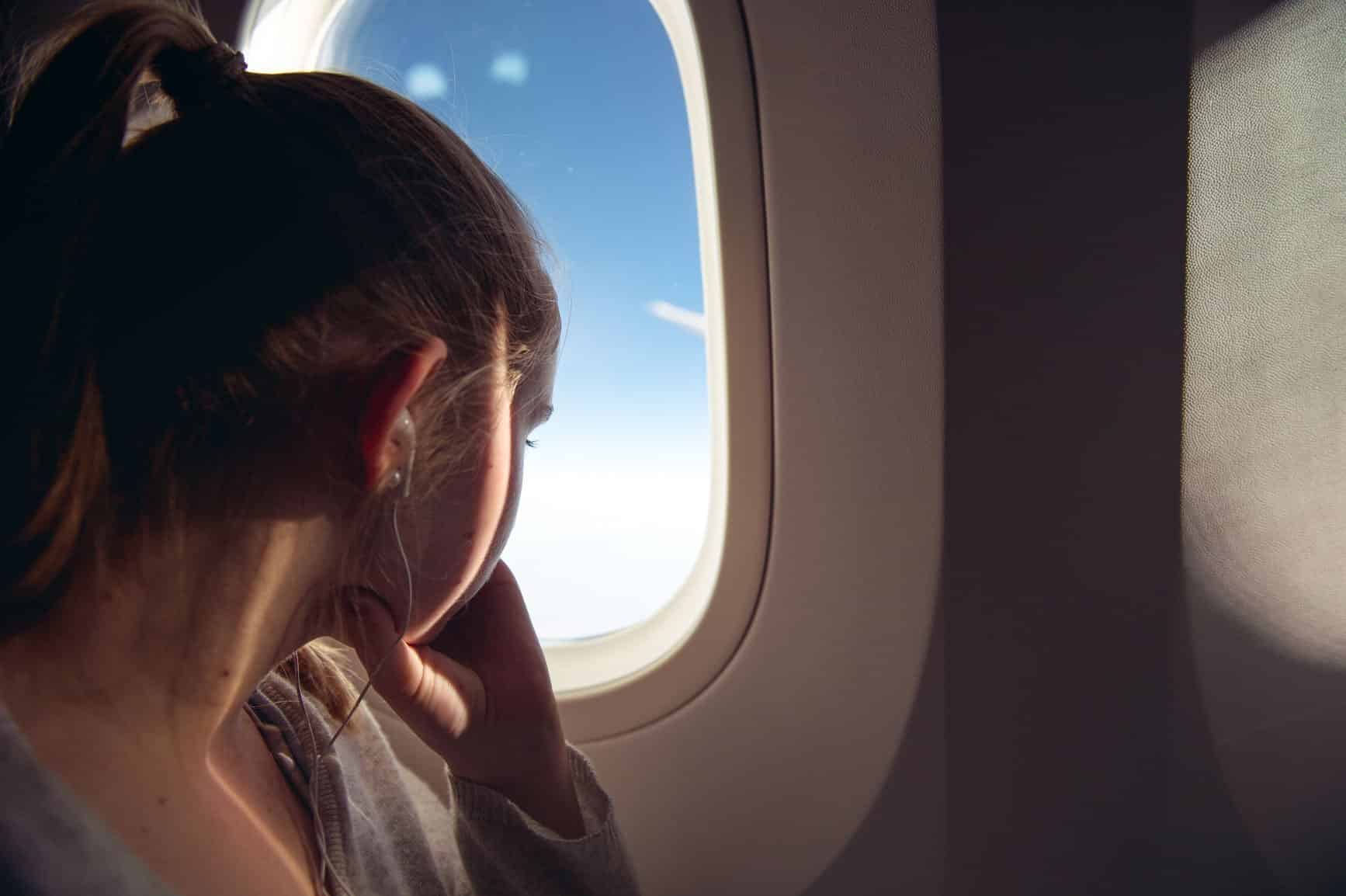 A woman listening to music and staring out of an airplane window.