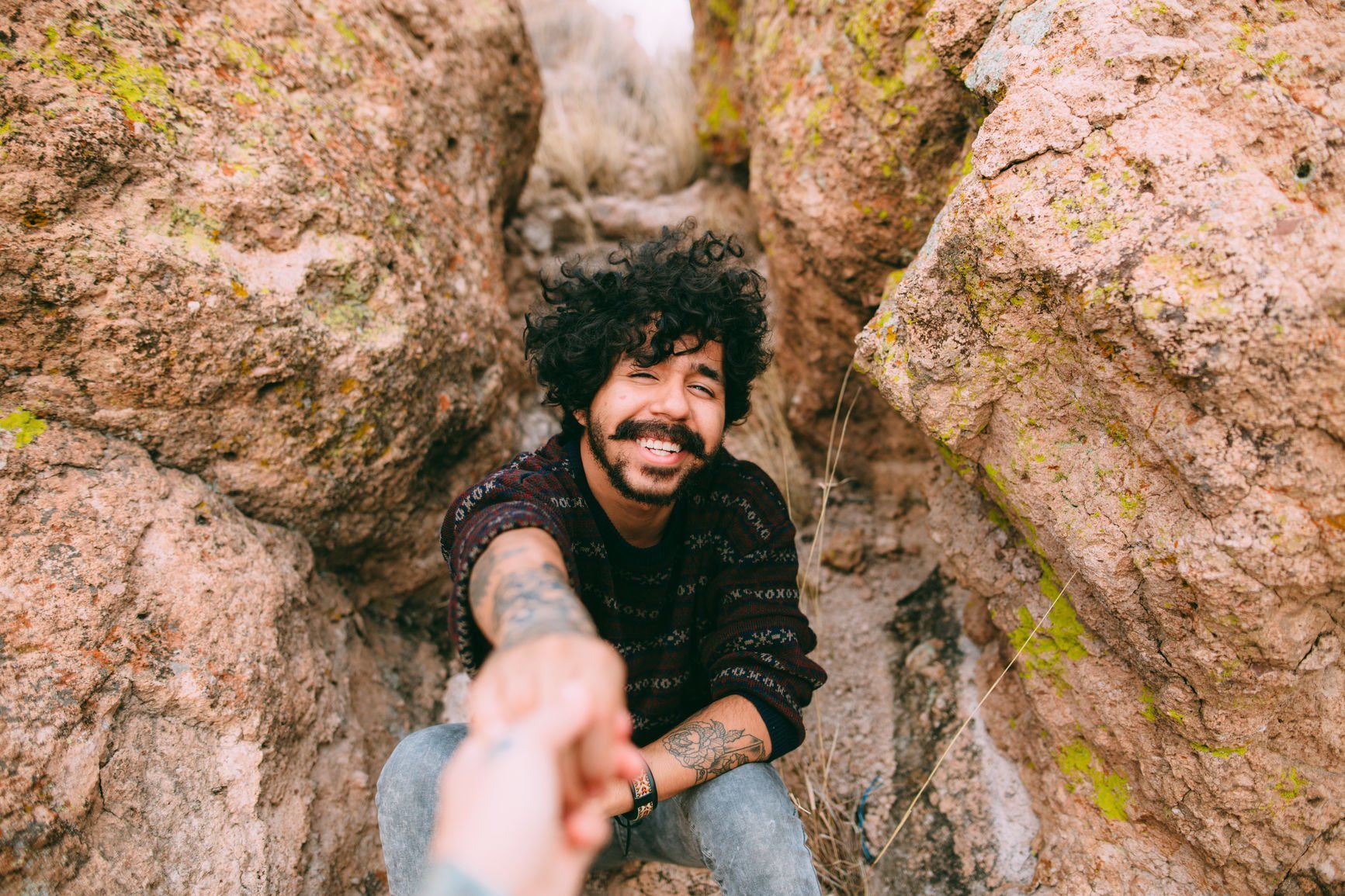 Man reaching out for a hand while climbing a mountain.