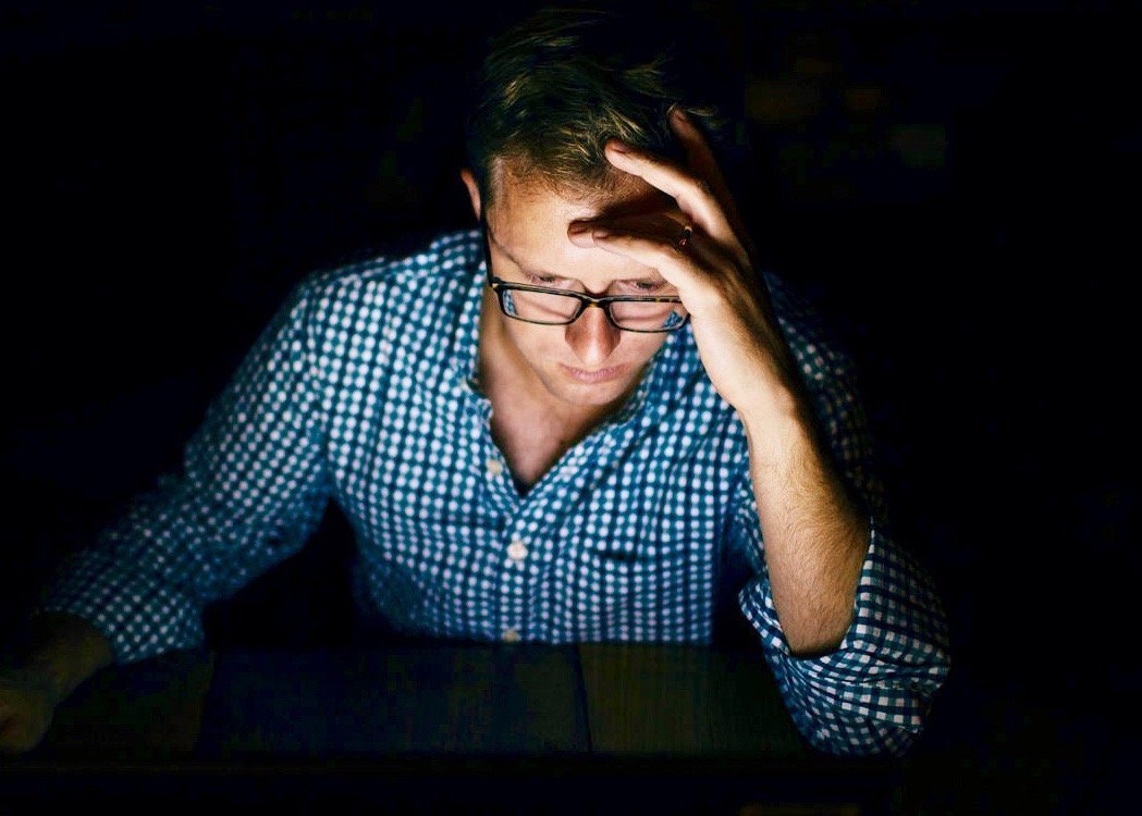 A man in the dark with his face illuminated by his computer.