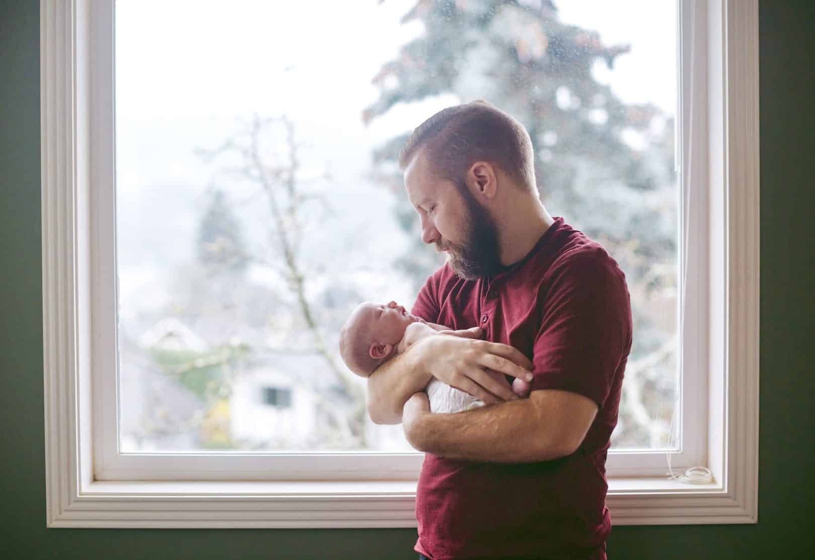 A new father holding his baby by a window.