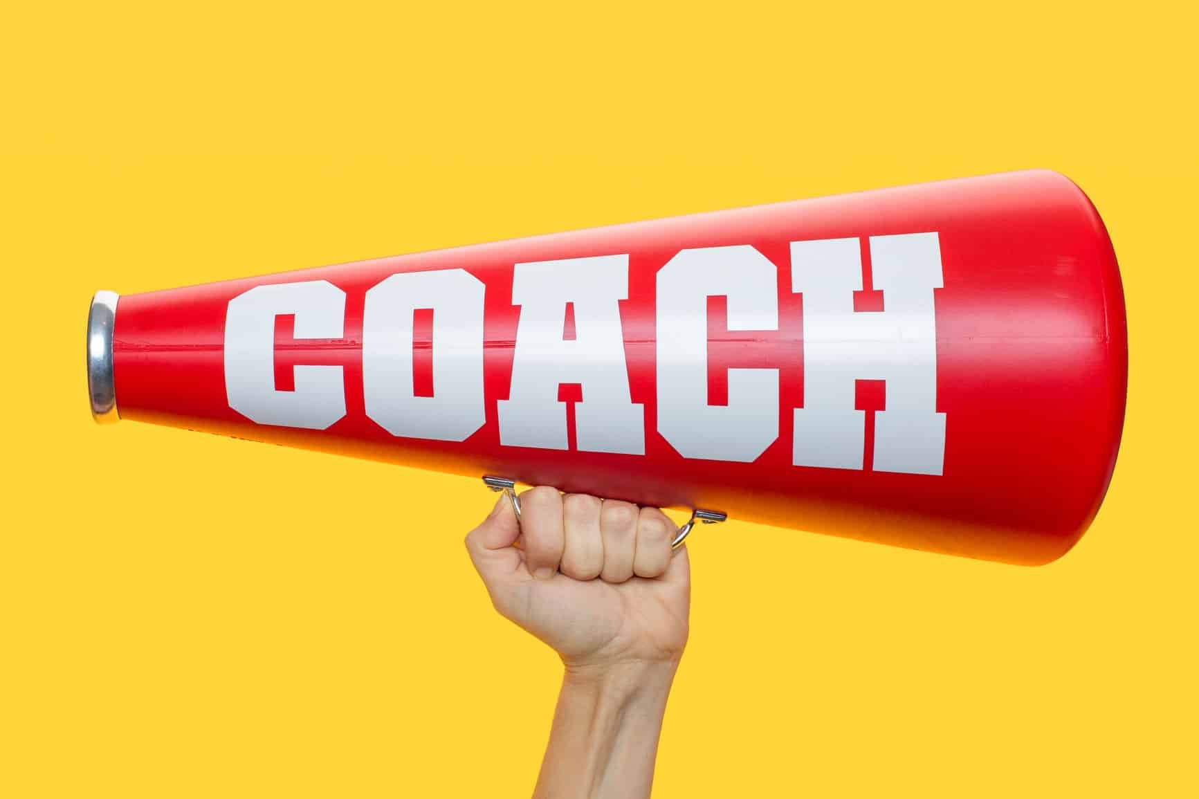 A hand holding a red megaphone that says "coach" on it.