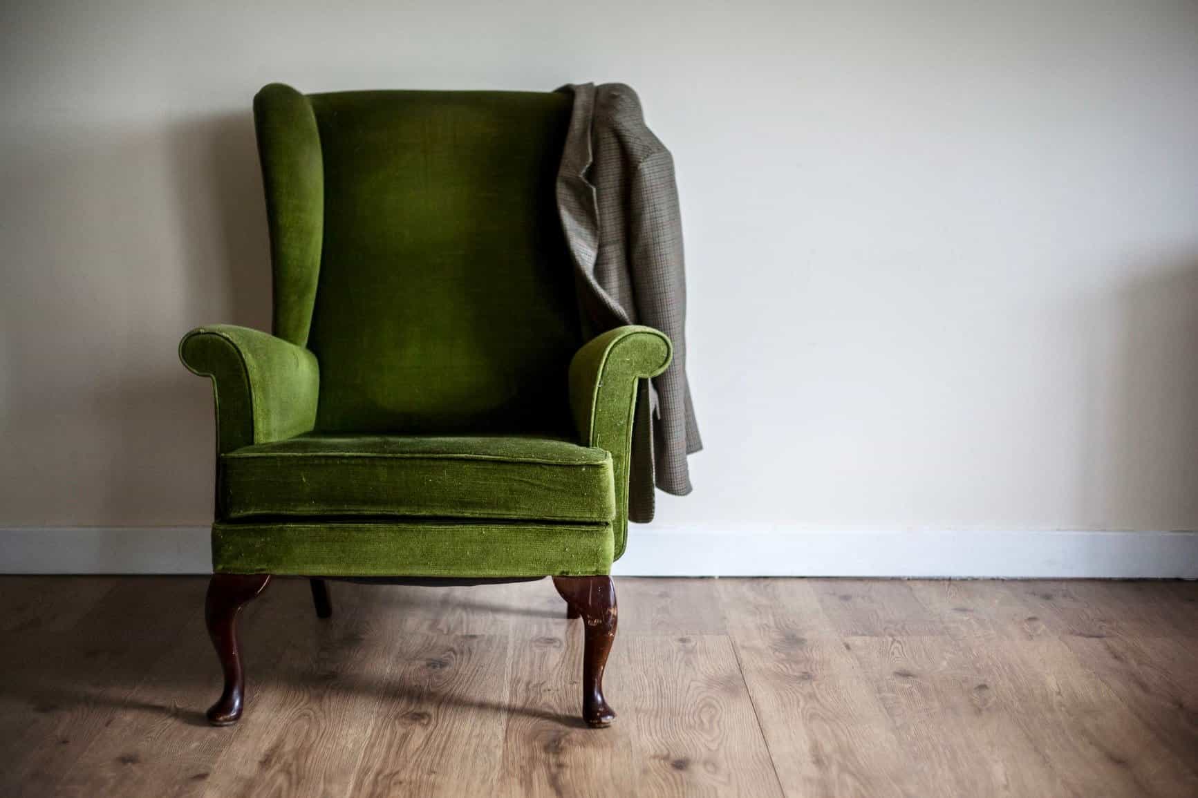 Old green velvet shabby chic chair sits alone in a room in natural light.