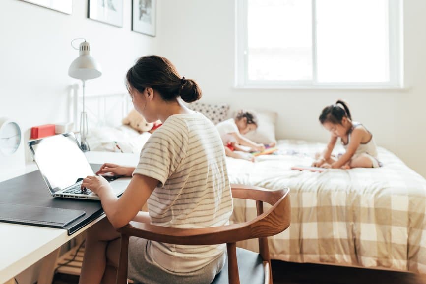 Mother Working At Laptop With Children In Background