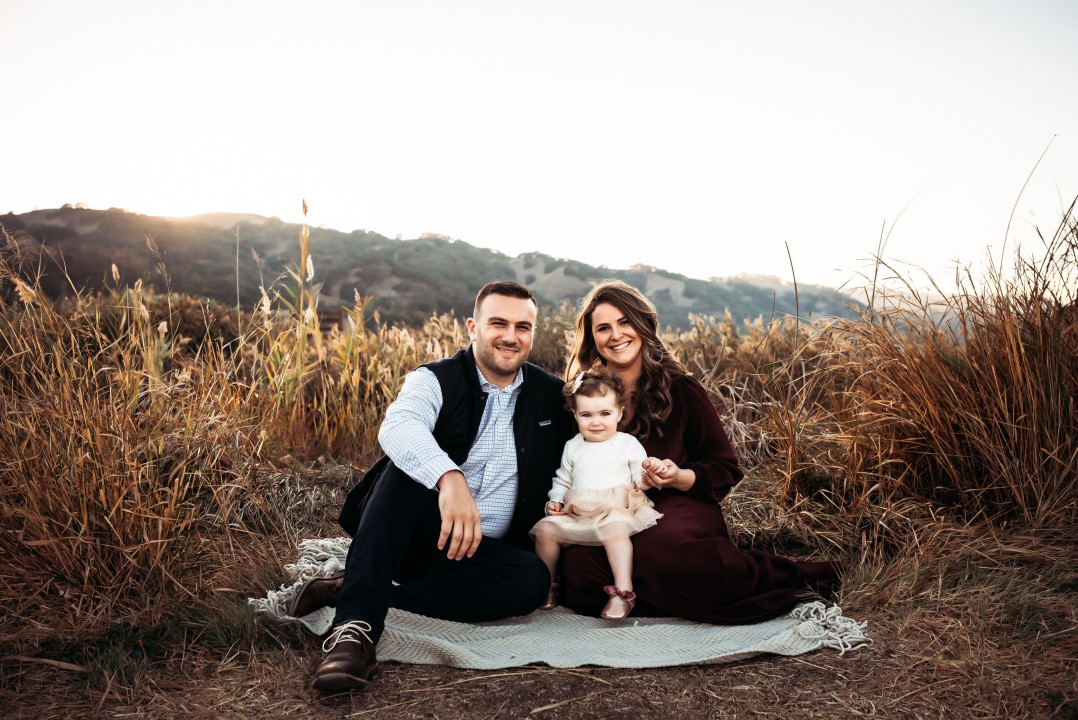 A family with their baby posing on a blanket in a field.