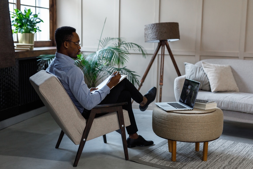 Side view of serious male doctor, using laptop for online therapy session with client and discussing problems with him.