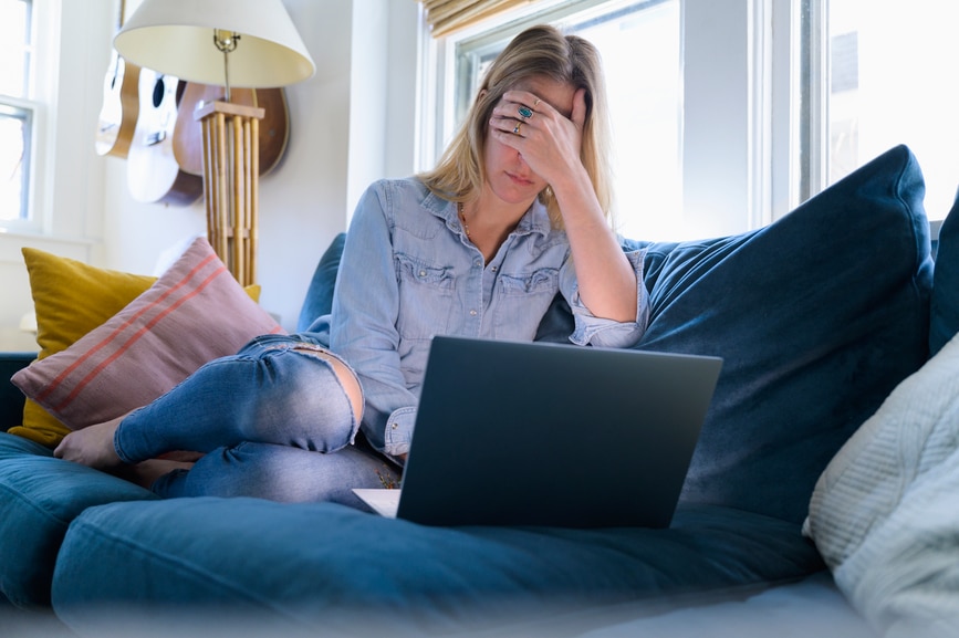 Woman At Laptop On Couch With Head In Hands