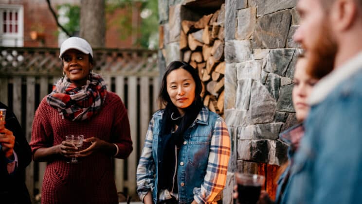 Stock photo of a group of friends chatting while enjoying the warmth of an outdoor fireplace during an outdoor get together with friends.