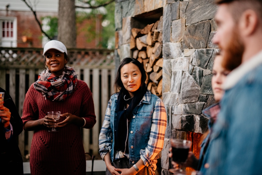 Stock photo of a group of friends chatting while enjoying the warmth of an outdoor fireplace during an outdoor get together with friends.