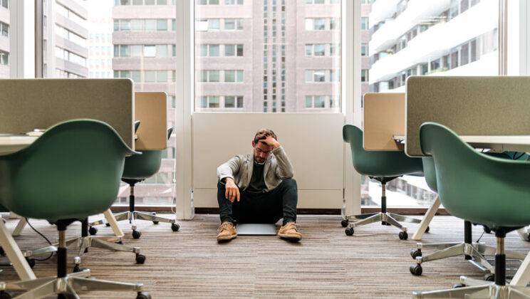 A man sitting on the floor of an office, looking distressed.