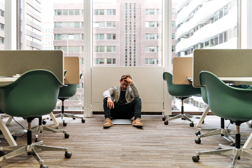 A man sitting on the floor of an office, looking distressed.