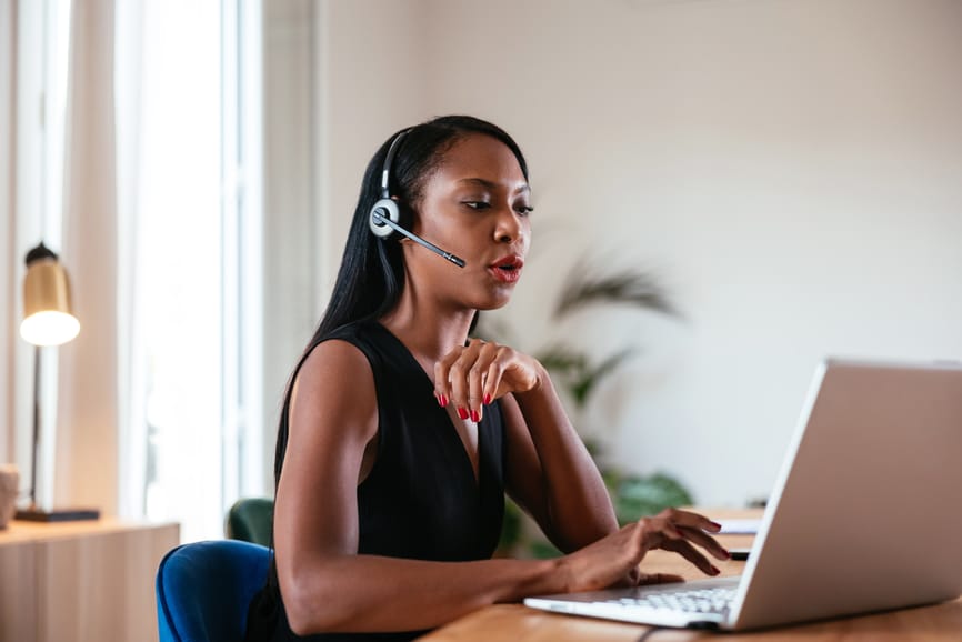 Young elegant African American female in headset having call while looking at screen of laptop