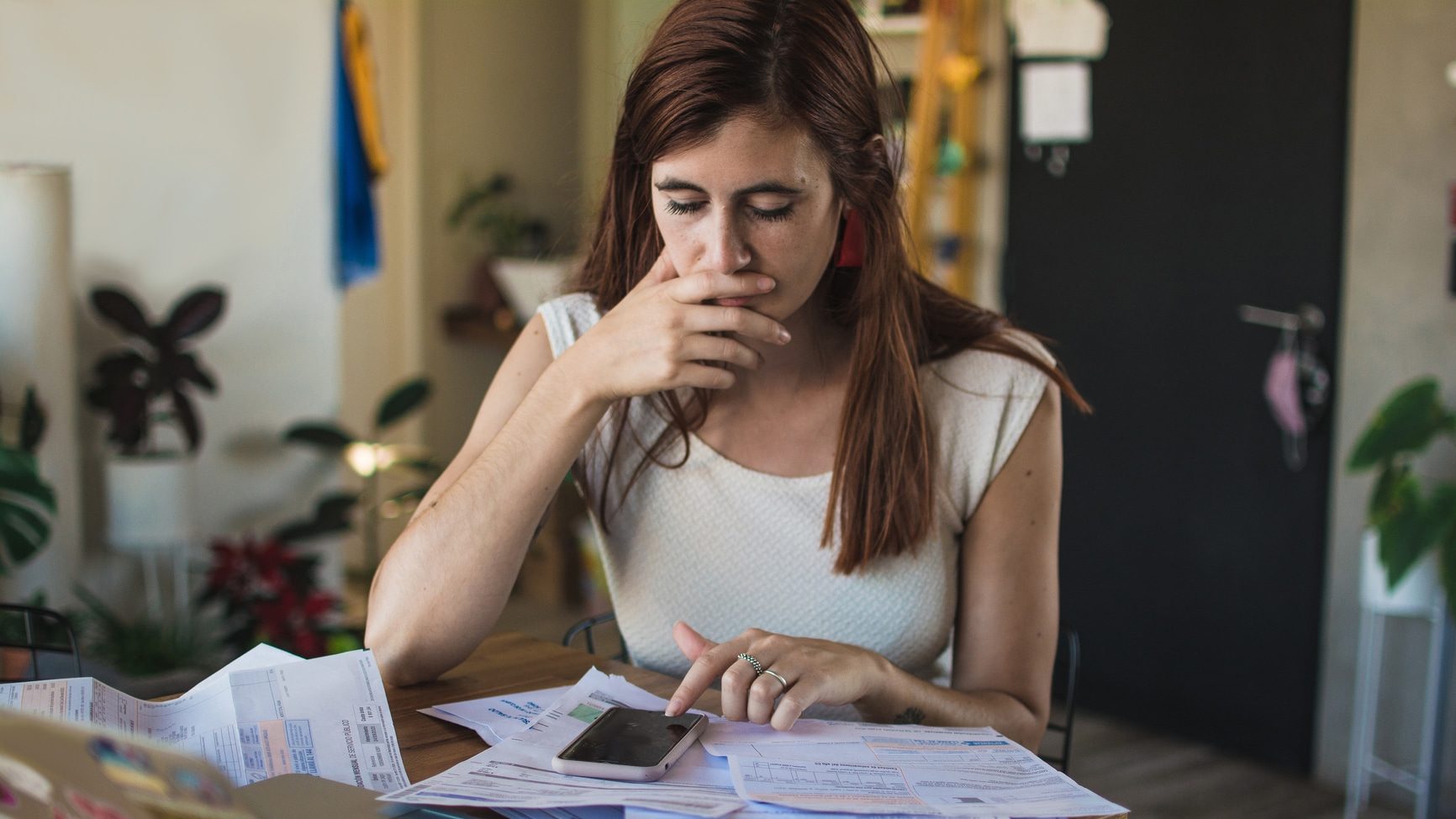 Young woman taking care of personal finance. She is sitting at a table with bills, laptop and her phone, working on numbers.