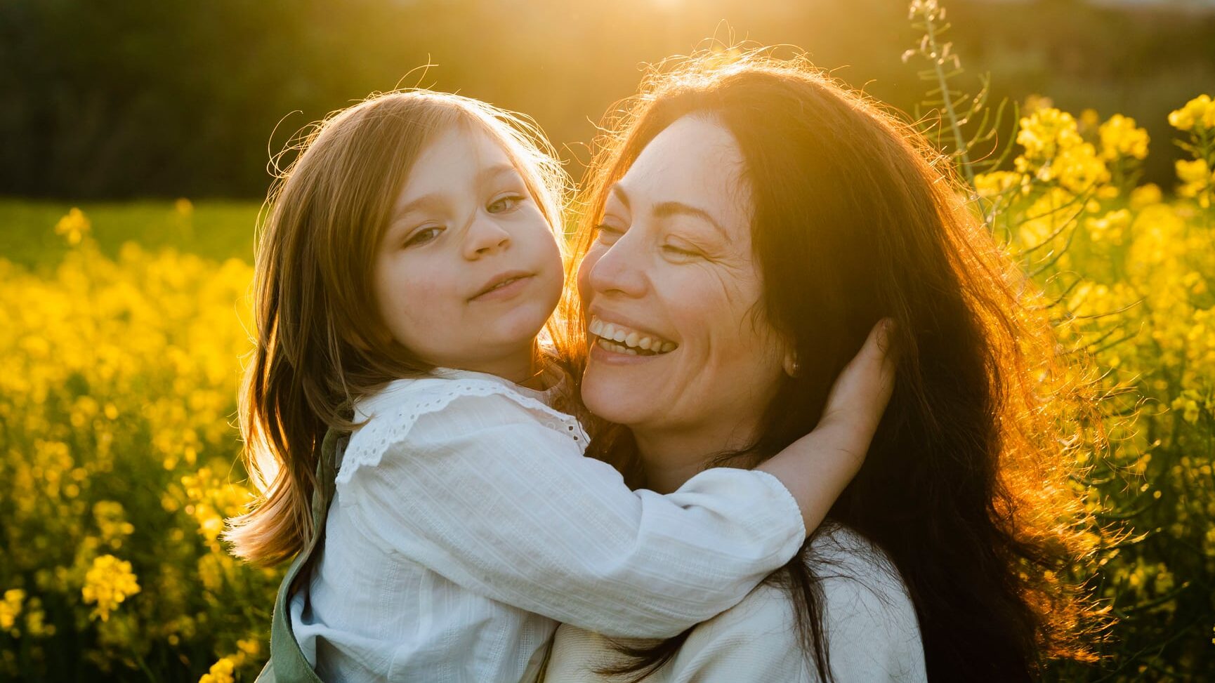 Mother holding her daughter in her arms while have fun together in the field in a sunset light.