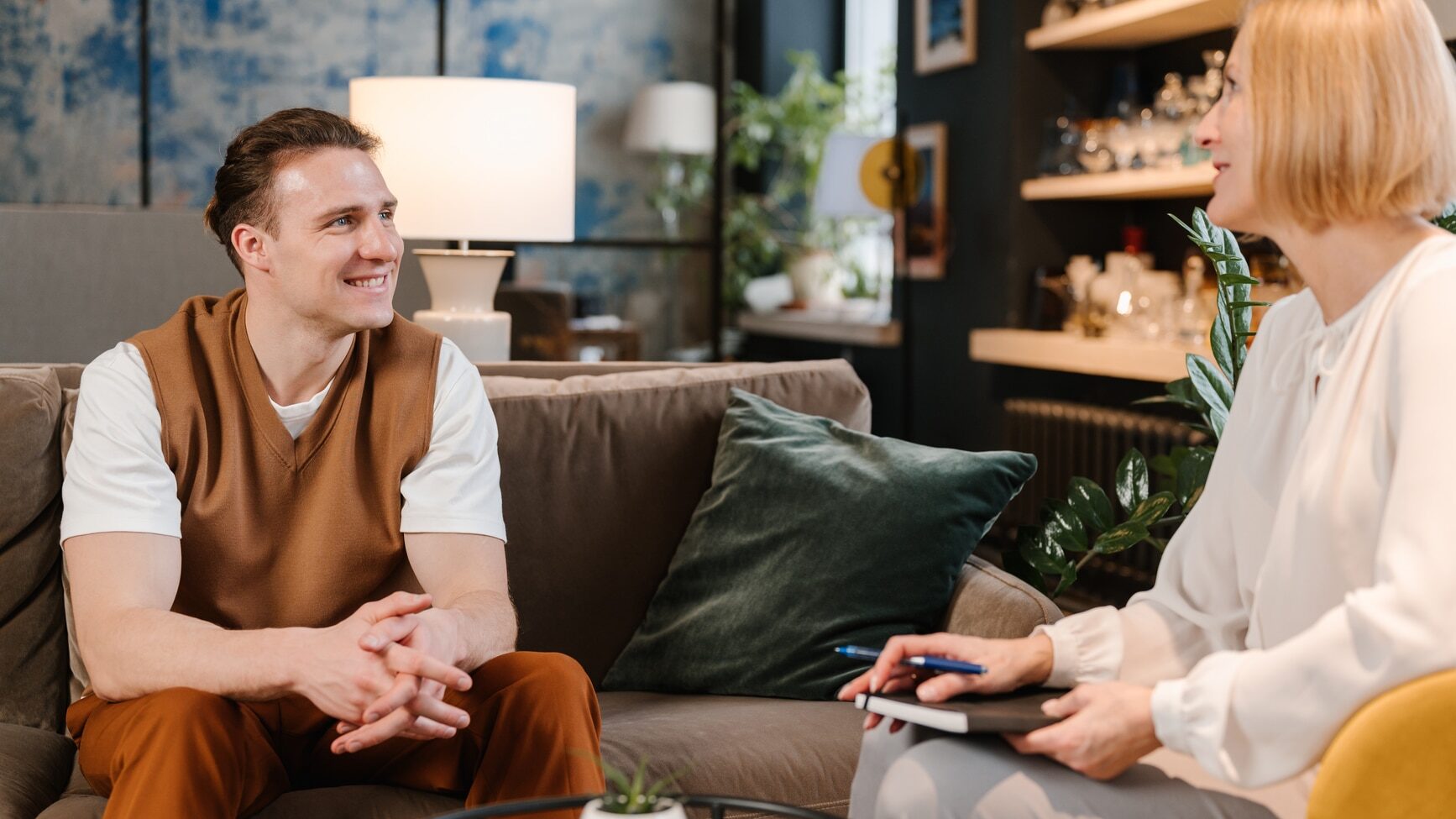 Content male patient siting on sofa and speaking to female counselor during psychotherapy consultation