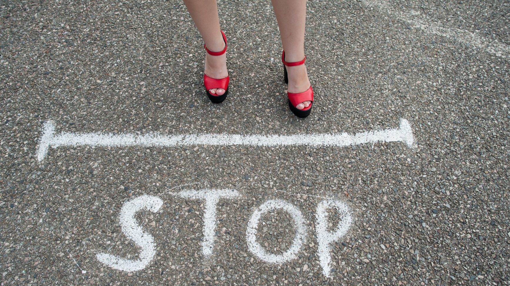 The legs of a young woman near the STOP sign painted on the asphalt