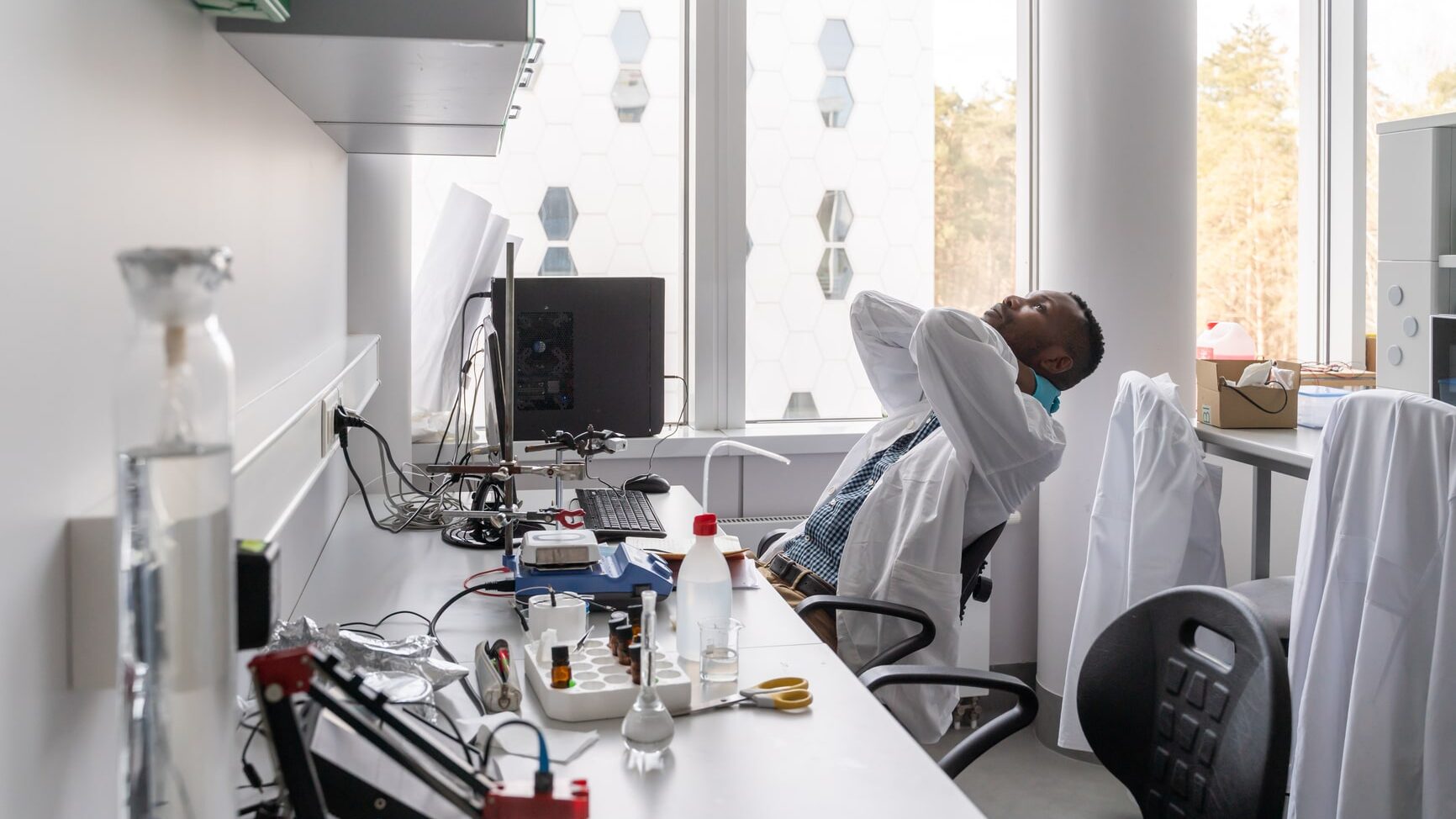 Photo Of Man Wearing Lab Coat In A Luminous Lab. He Is Tired.