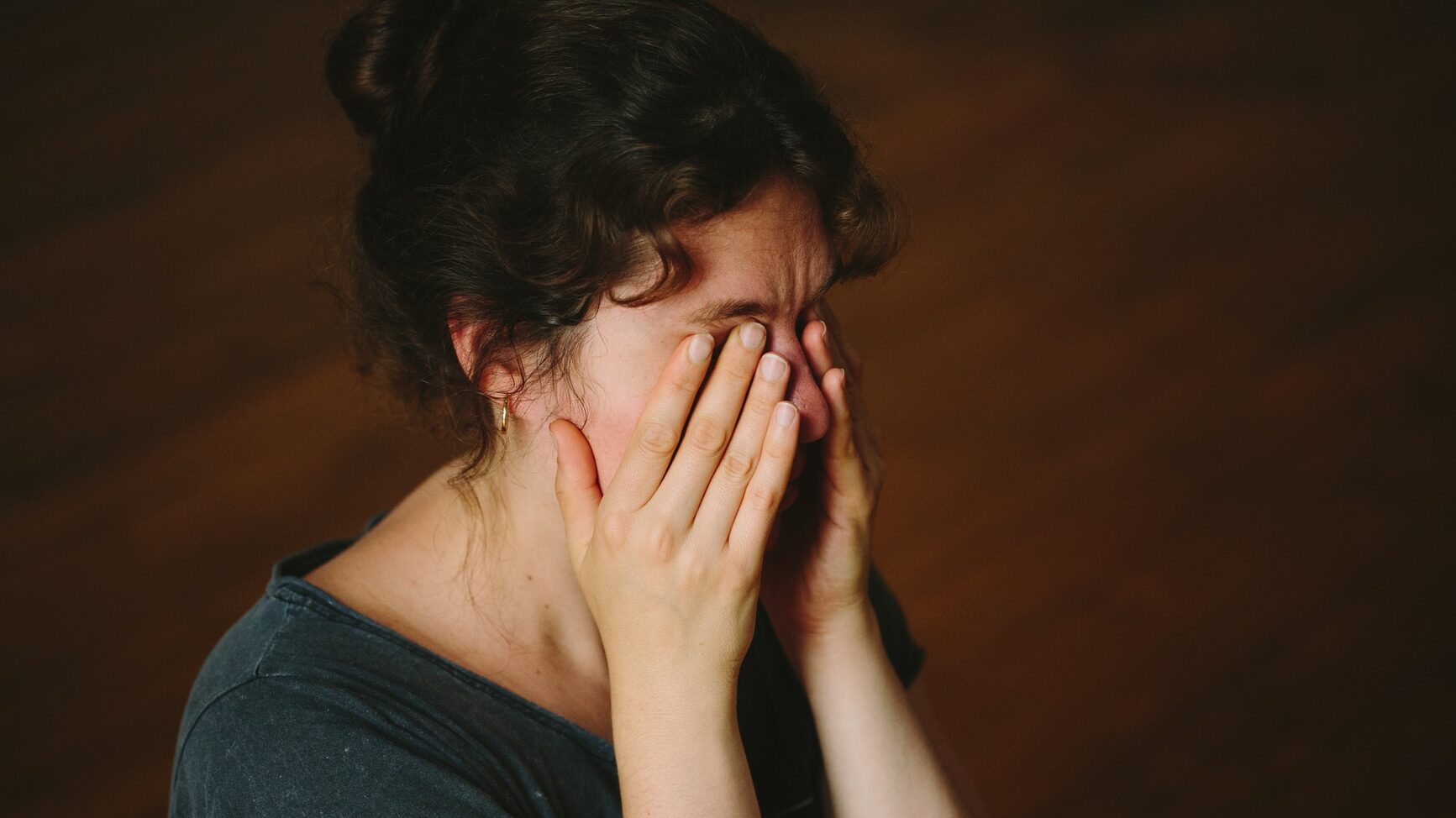 A close up of a person rubbing their eyes, forehead and temples with their hands