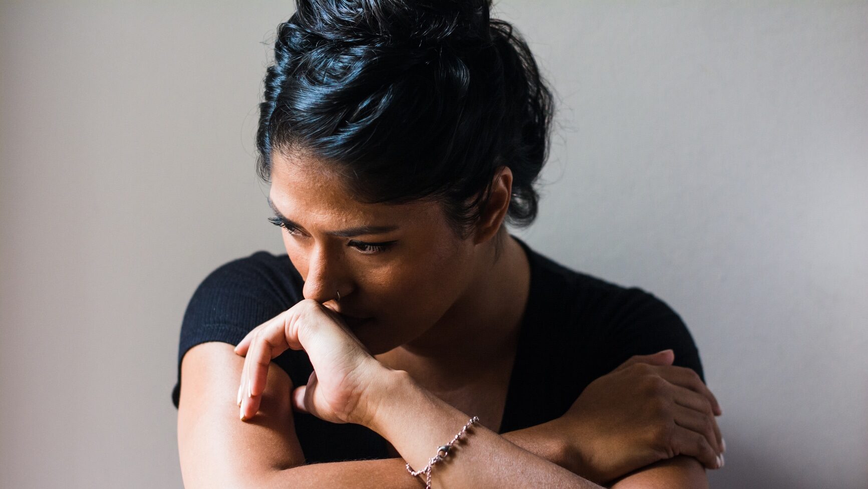 Woman portrait displaying subtle emotions portrait. She is sitting against a white wall indoors.