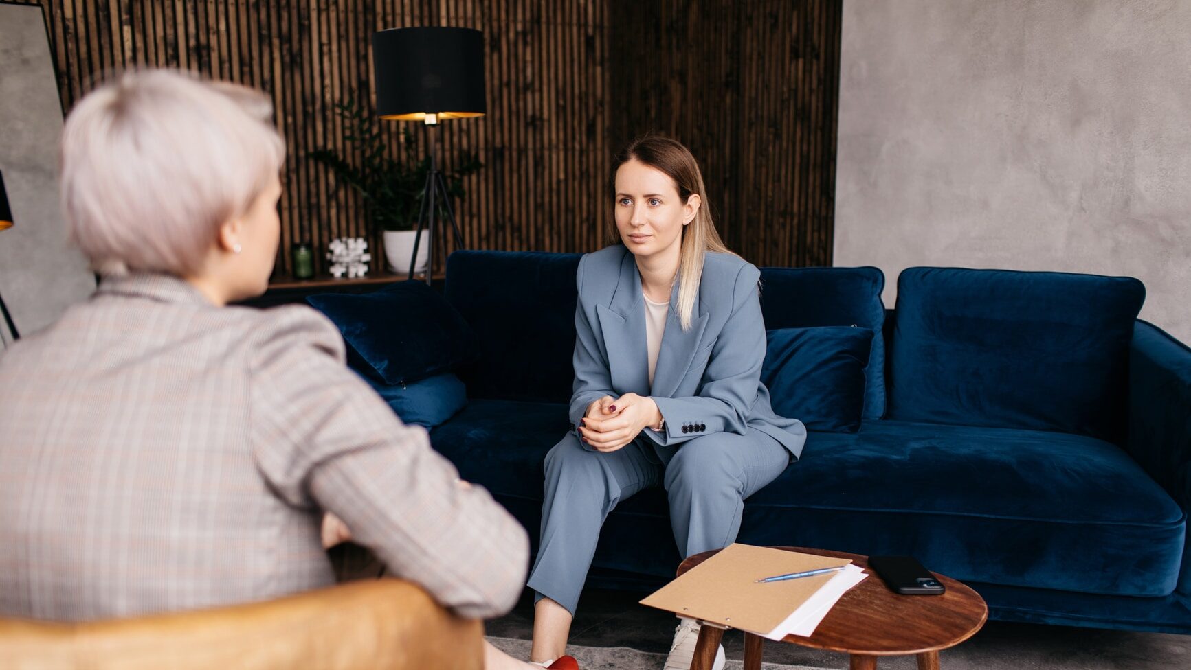 Female patient sitting on sofa and taking to psychotherapist while discussing mental issues during appointment