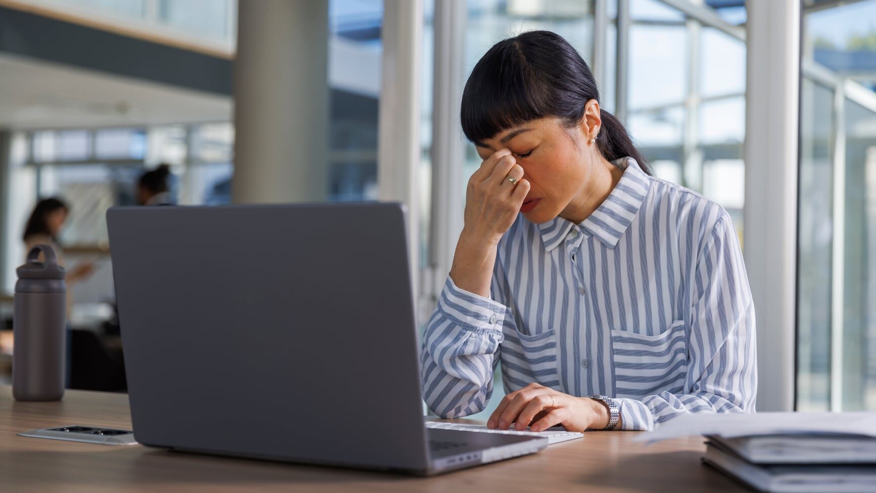 Tensed businesswoman with laptop at desk. Overworked female manager is in corporate office. She is sitting with eyes closed.