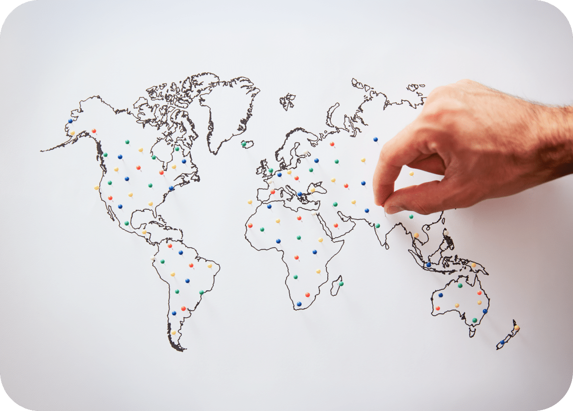 A hand places a pin on a world map filled with colorful dots, each marking various locations across different continents.