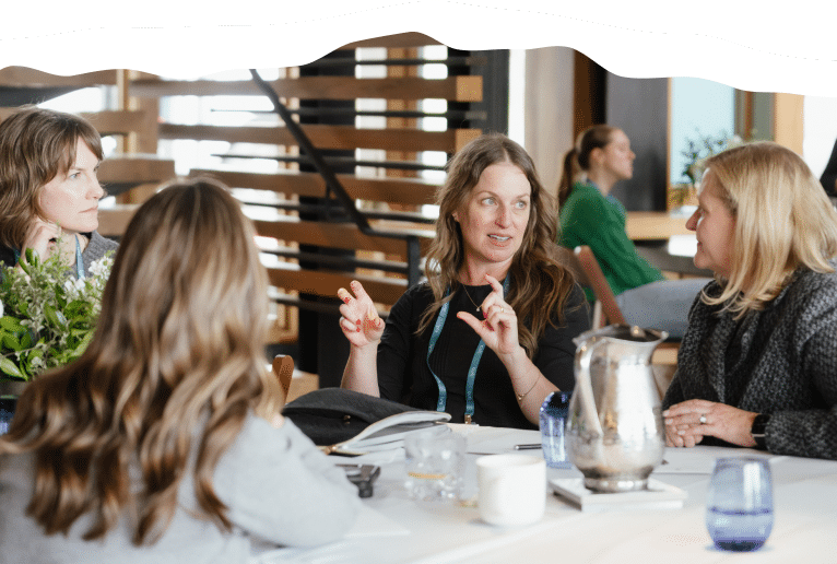 four women at a table speaking to each other