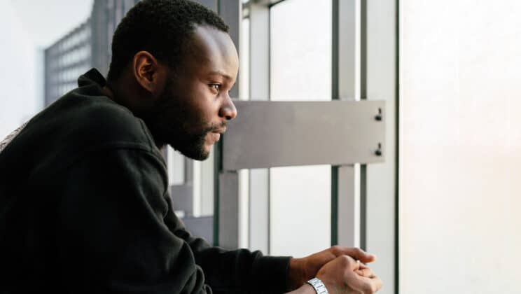 Young black man with pensive expression looking out window