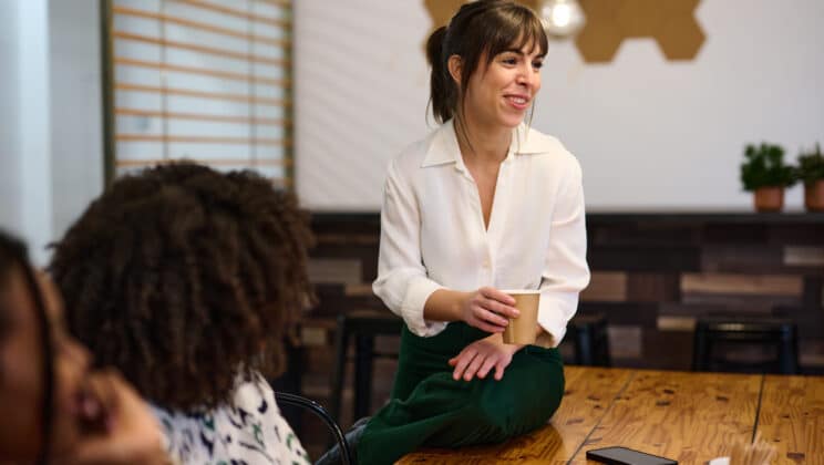 A businesswoman with a bright smile participates in a team meeting, holding a coffee cup, in a contemporary office space