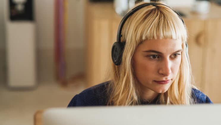 Close up of young blond woman with headphones sitting in front of the computer
