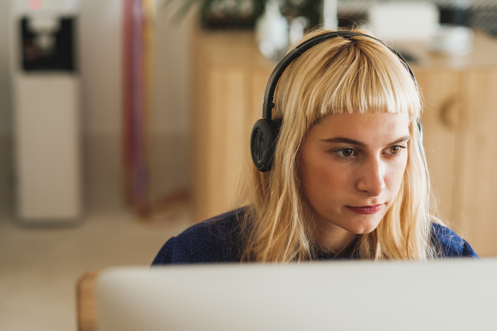 Close up of young blond woman with headphones sitting in front of the computer
