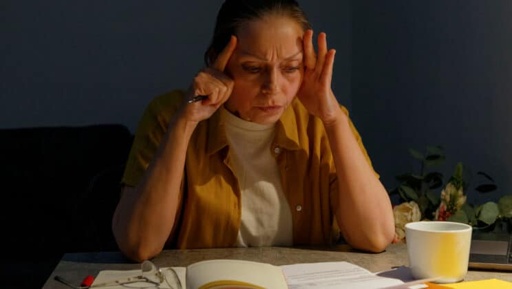 Exhausted middle aged woman touching head and thinking while reading document during work at home at night