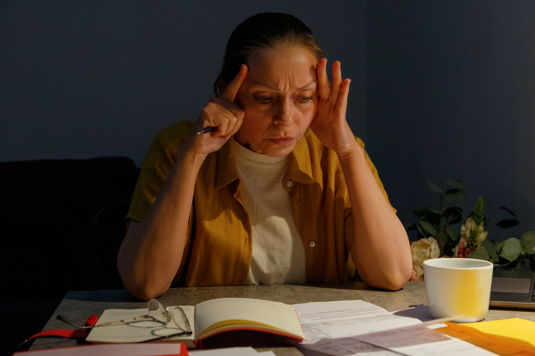 Exhausted middle aged woman touching head and thinking while reading document during work at home at night