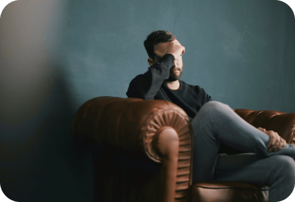 man putting hand to his forehead sitting on a brown couch