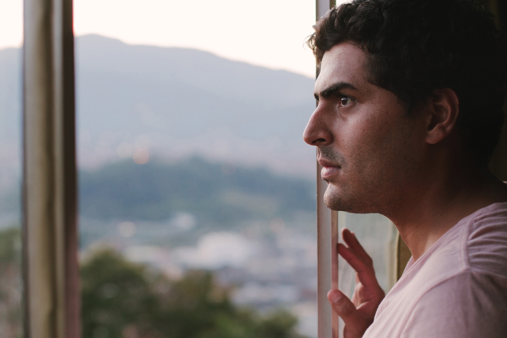 A man looks out through a window at a distant mountain landscape.